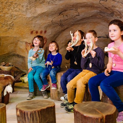 Fünf Kinder sitzen mit tierischen Knochen auf Baumstämmen in einer Höhle im Neanderthal Museum in Mettmann