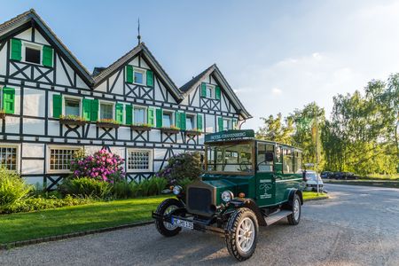 Ein grüner Oldtimer parkt vor einem Fachwerkhaus, in dem das Hotel Gravenberg untergebracht ist.